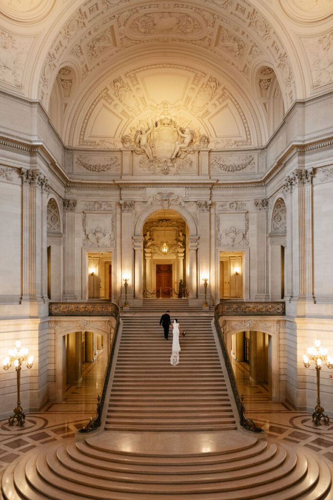 A wedding couple walking up a grand staircase in City Hall 
