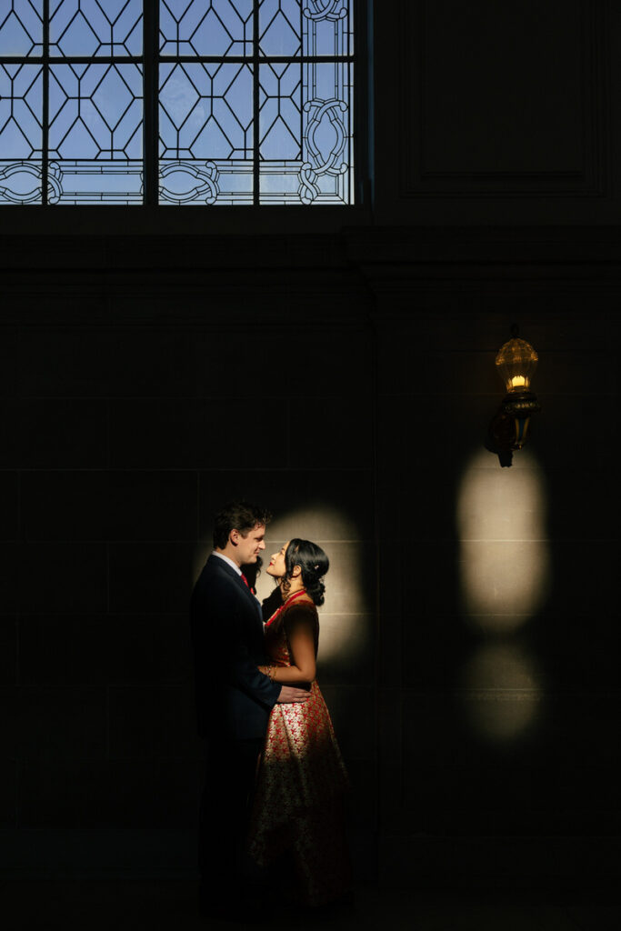 A newlywed couple standing in a small slip of light in City Hall