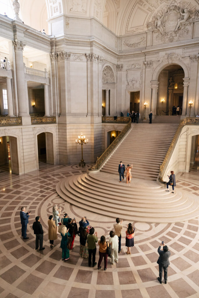 A wedding couple walking down a grand staircase towards celebrating wedding guests 