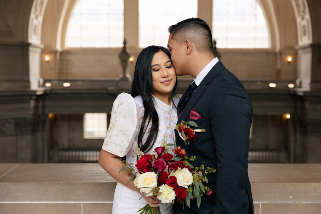 A person kissing their partner's head on their wedding day 