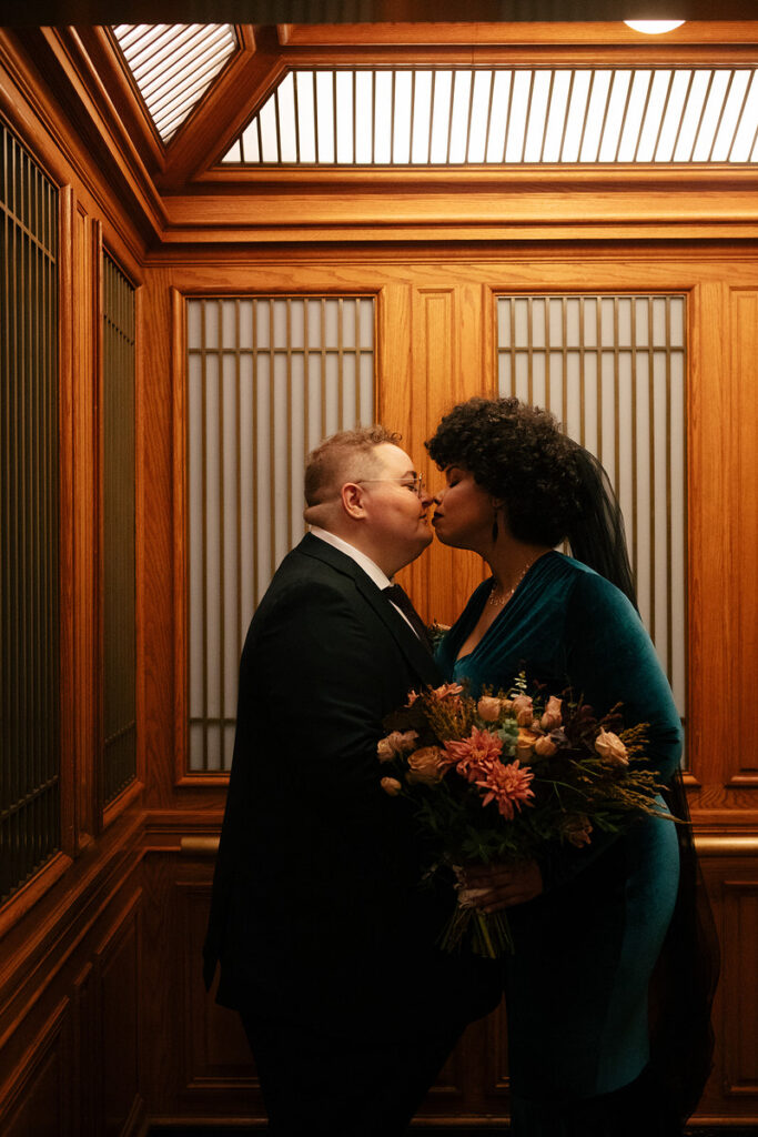 A newlywed couple about to kiss inside of a vintage style elevator 