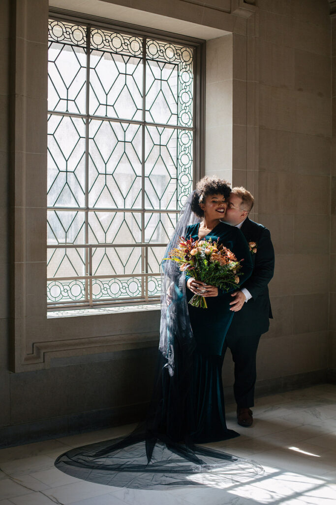 A person standing behind their partner kissing their cheek 