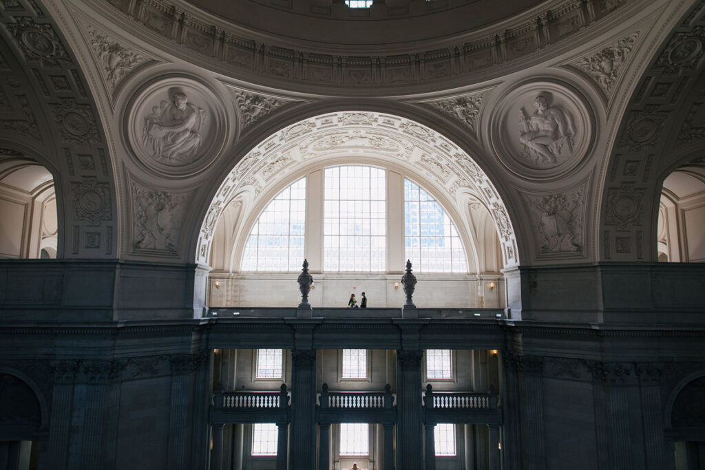 View from across the room of a couple standing inside a grand hallway in City Hall 