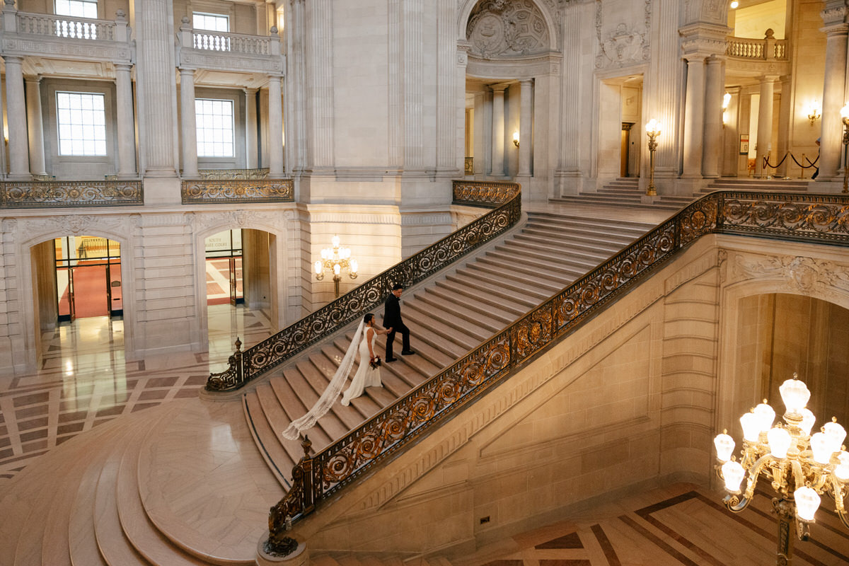 A wedding couple walking up a grand staircase during their San Francisco City Hall wedding