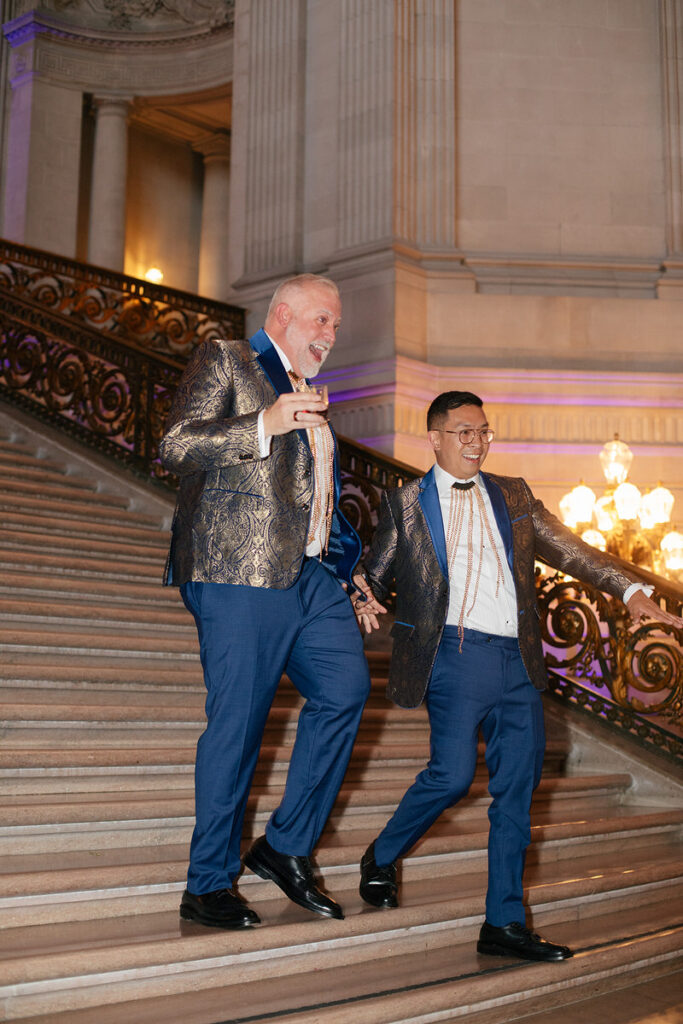 A newlywed couple laughing and walking down a staircase together 