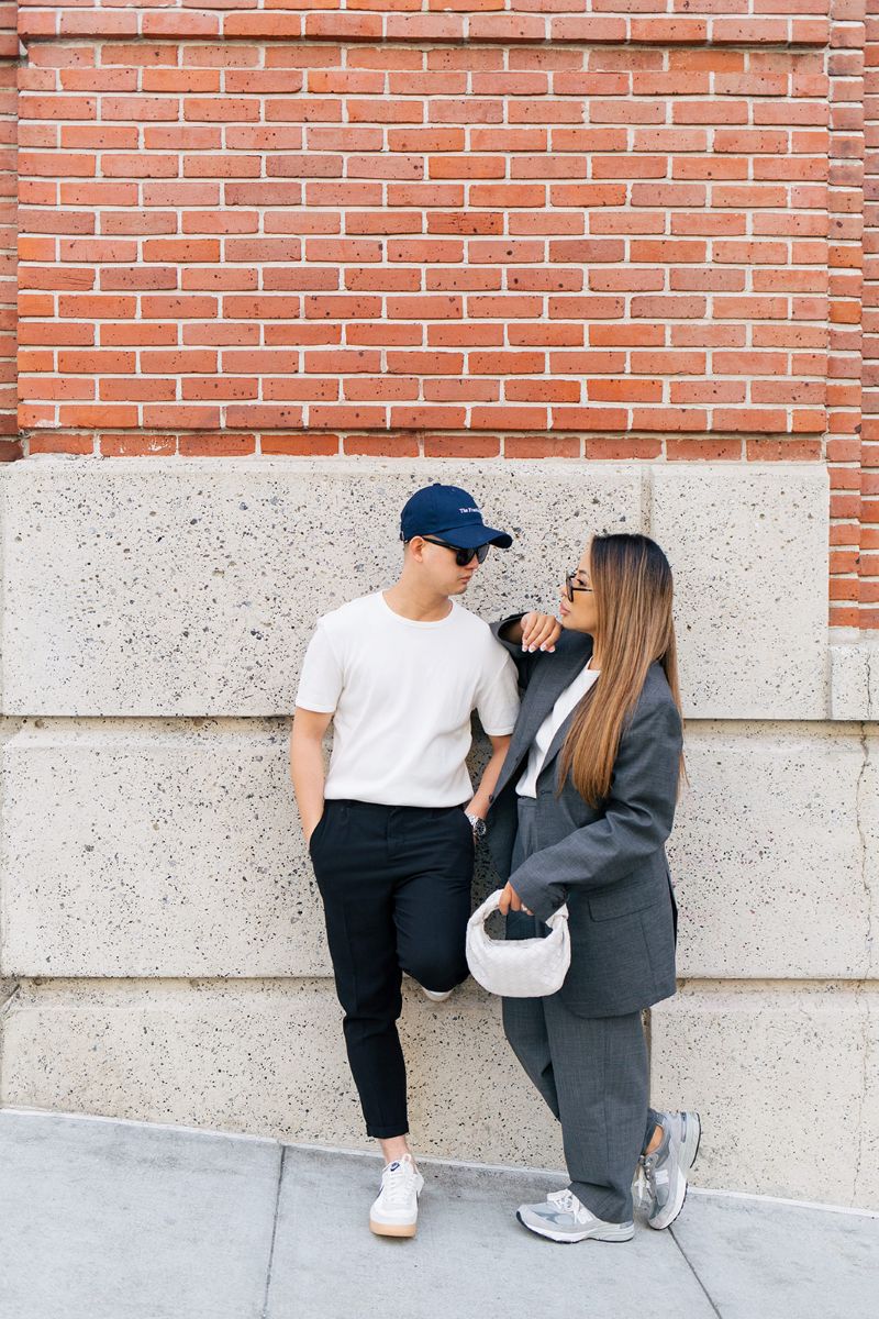 a couple in front of a brick wall leaning on one another and looking at each other