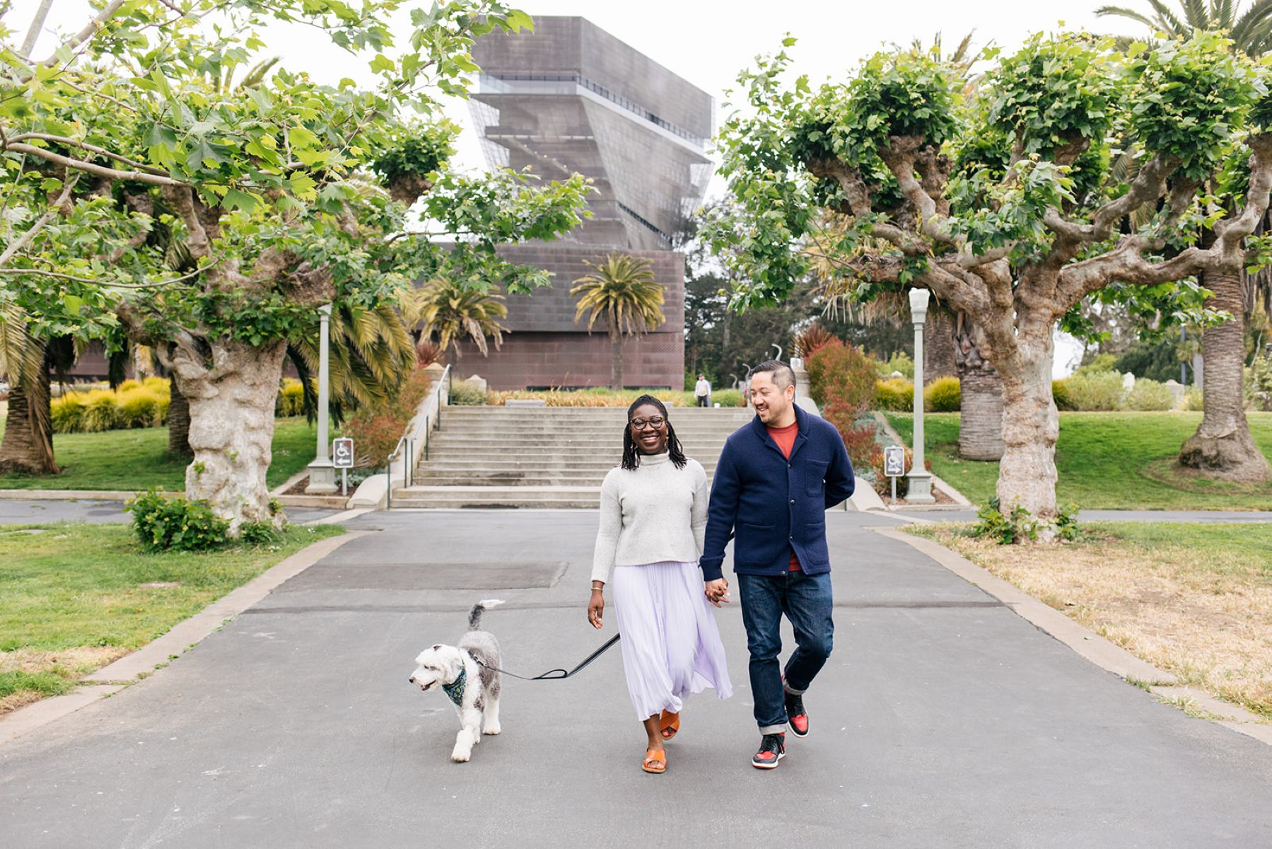 a couple holding hands and walking with their dog for an engagement session in san francisco
