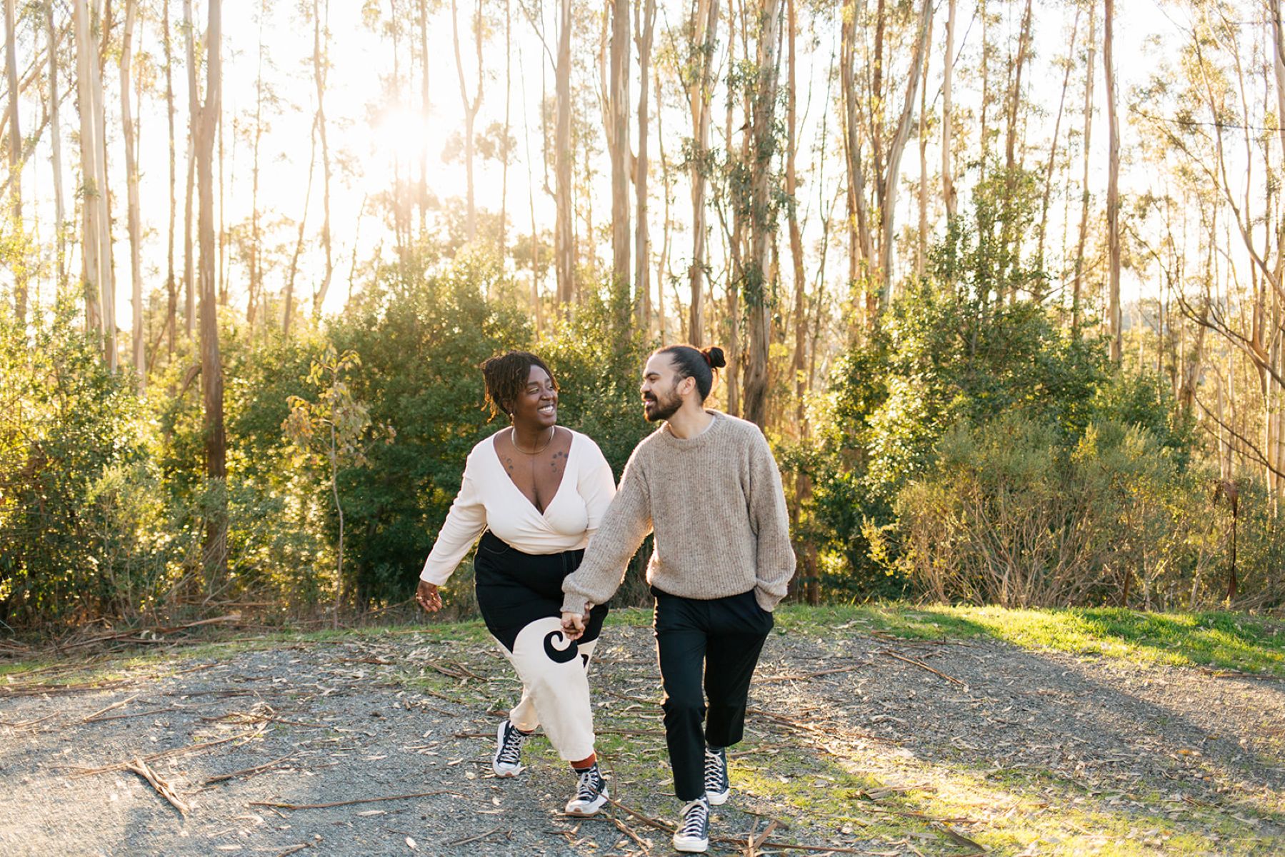 a couple walking hand in hand smiling at each other out in the woods