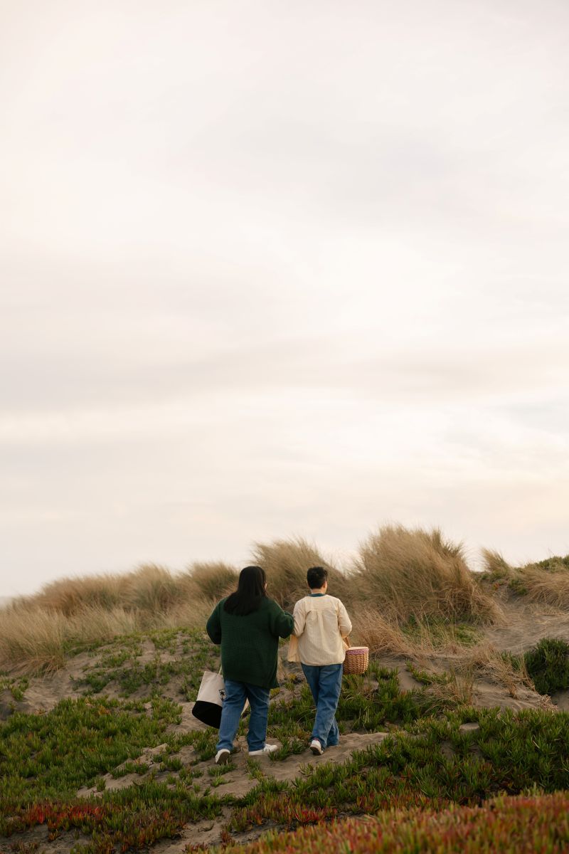 a couple walking hand in hand to have a picnic on the beach together next to the ocean