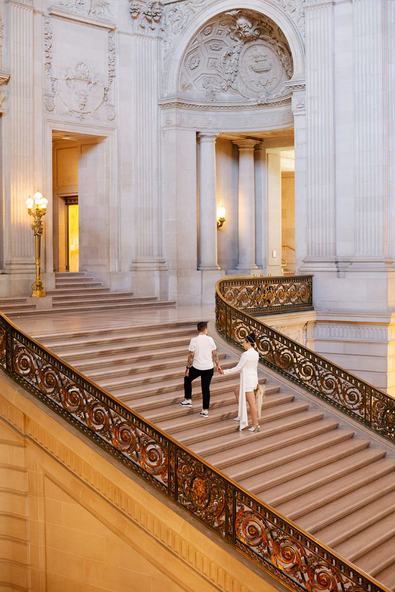 a couple walking up the grand staircase in san francisco city hall holding hands
