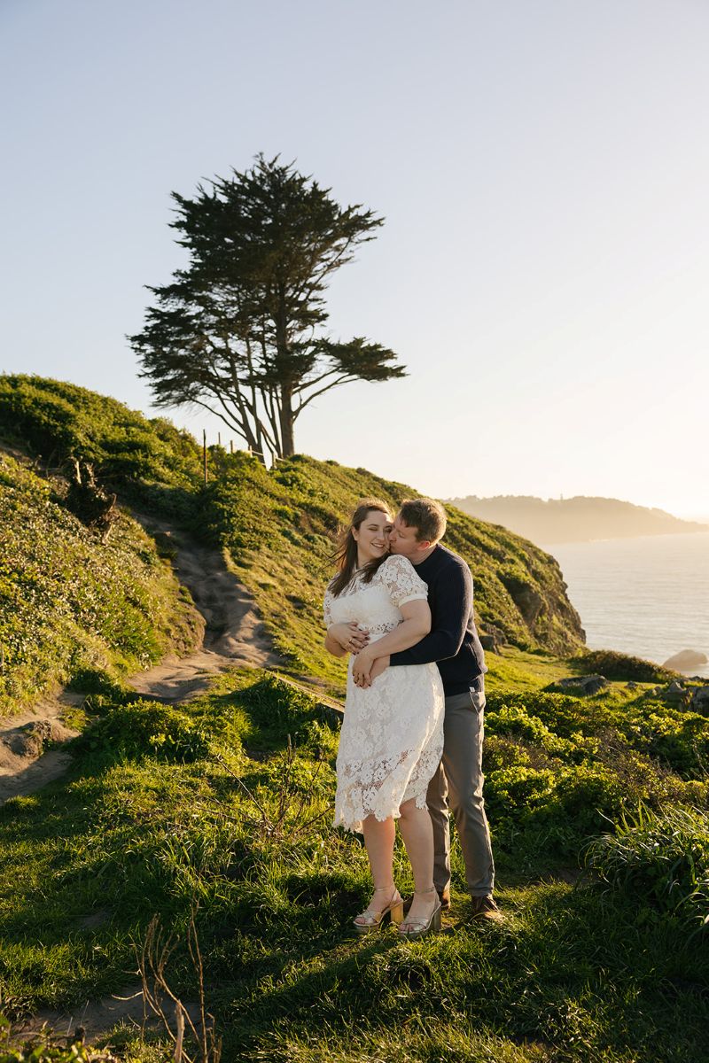 a man hugging his partner from behind and kissing her on the cheek at battery godfrey in san francisco