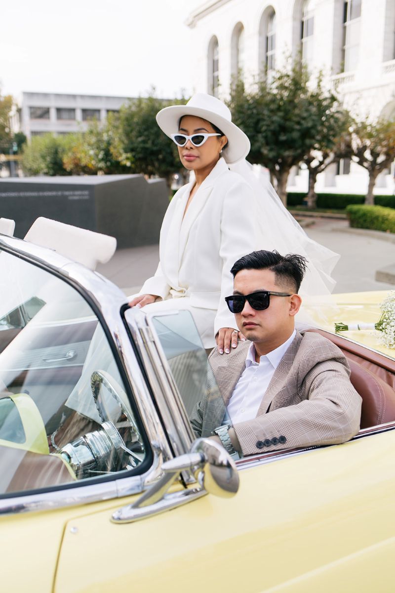a couple sitting inside of a yellow vintage car taking engagement photos the woman has her hand on her partner's shoulder