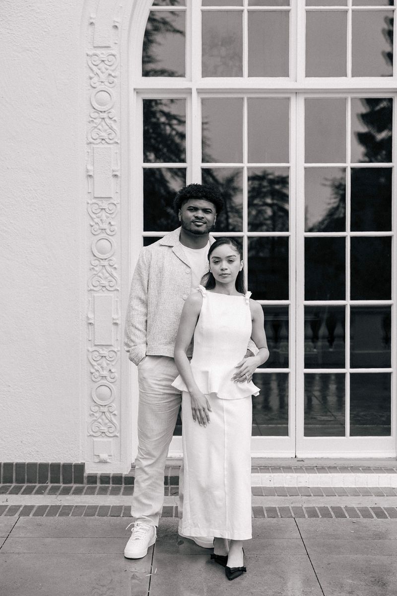 a couple taking engagement photos in front of villa montalvo they are both standing in front of a window