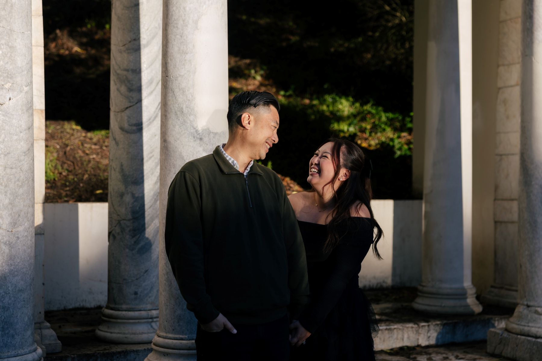 a couple taking engagement photos at portals of the past in golden gate park standing in front of large columns and smiling at each other