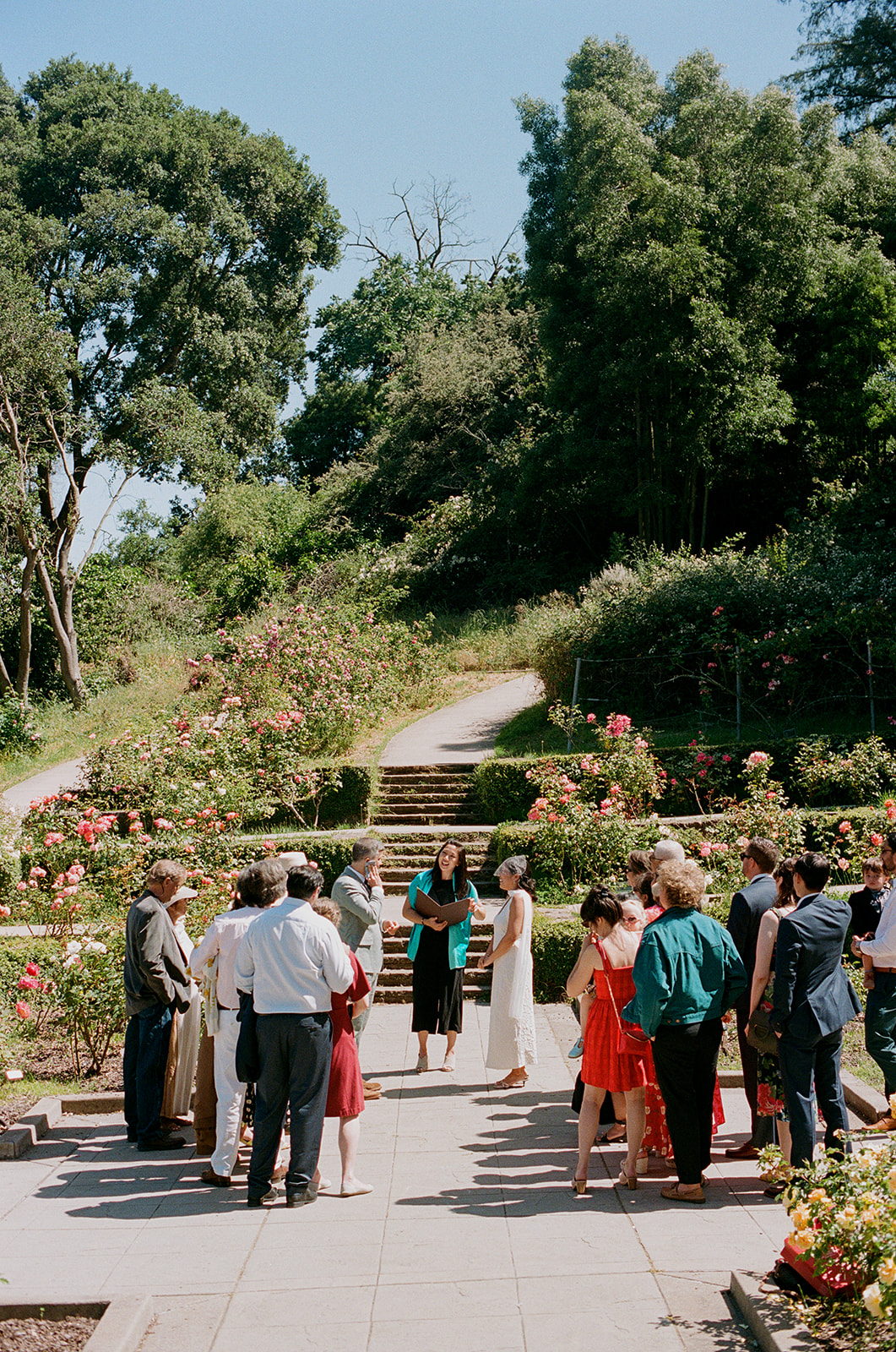 a couple at their wedding ceremony in a park surrounded by flowers with their wedding guests 