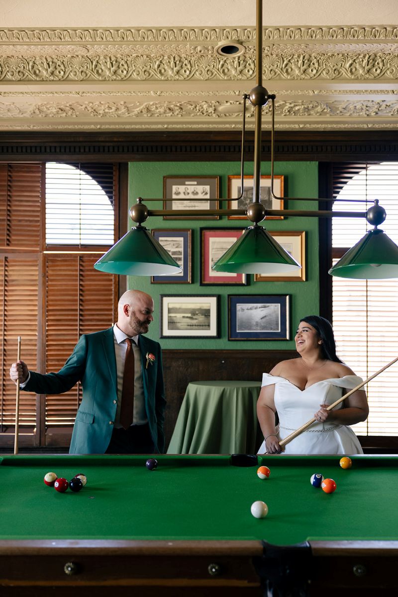 a couple playing pool in the pool room at the University Club of San Francisco on the day of their wedding 