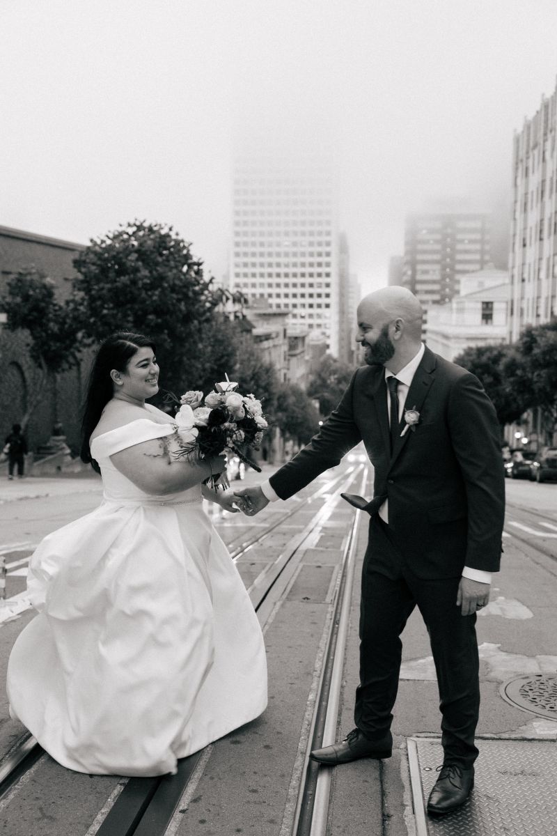 a couple crossing the tram tracks in san francisco on the day of their wedding as they take couple wedding portraits 