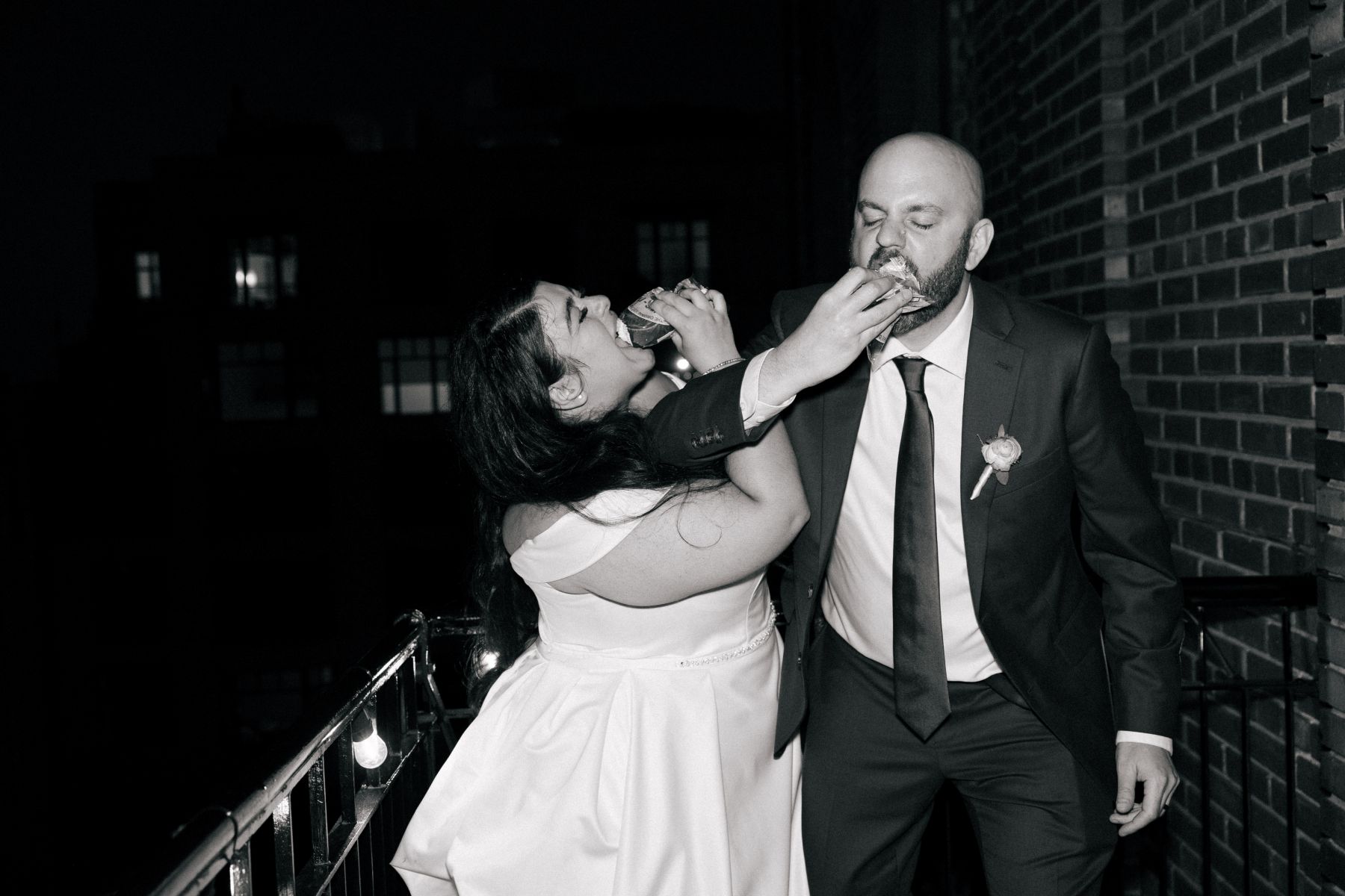 a couple crossing arms with each other at their wedding reception and feeding each other a piece of cake 