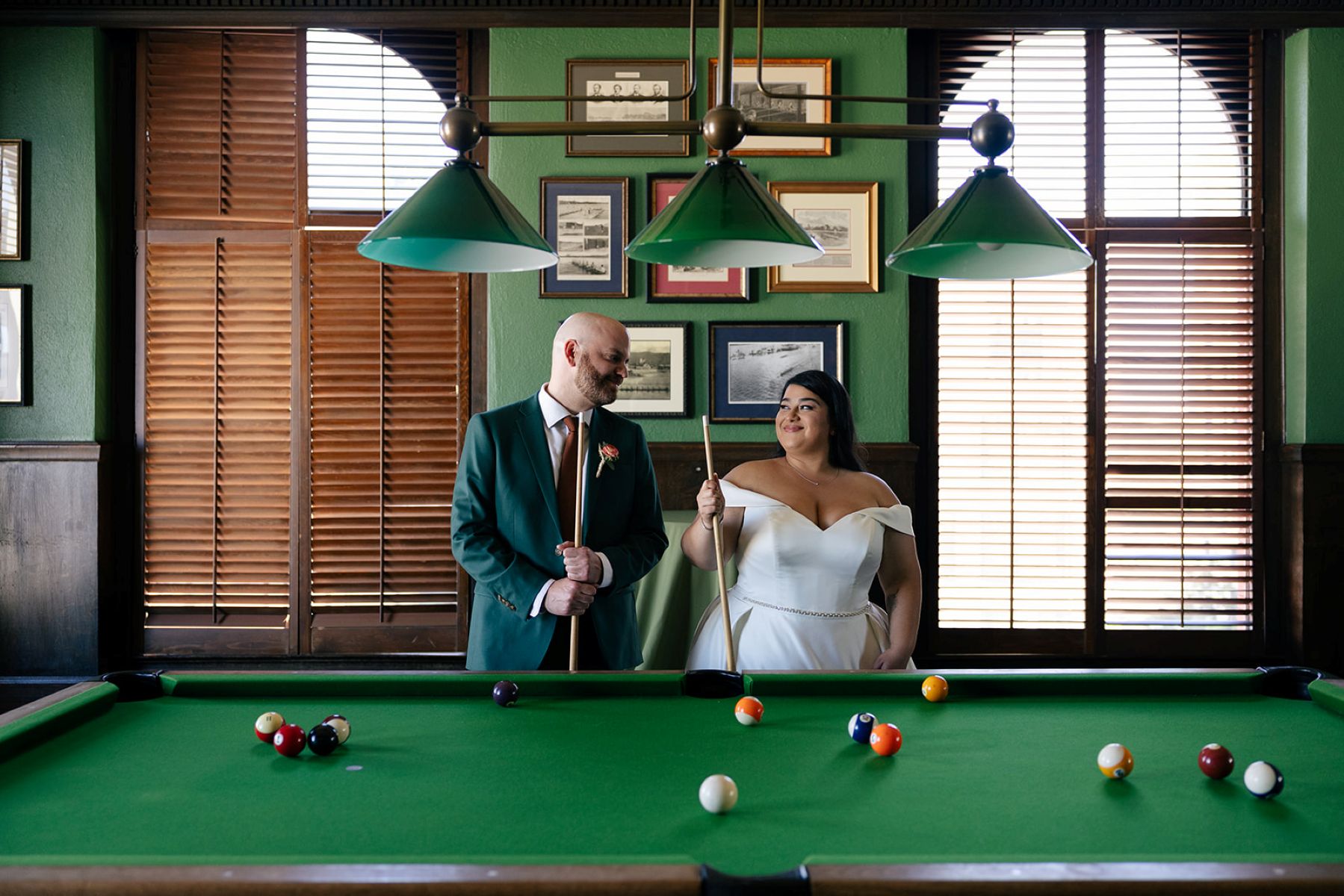 a couple smiling at each other and holding pool sticks in front of a pool table at the University Club of San Francisco where they are having their wedding