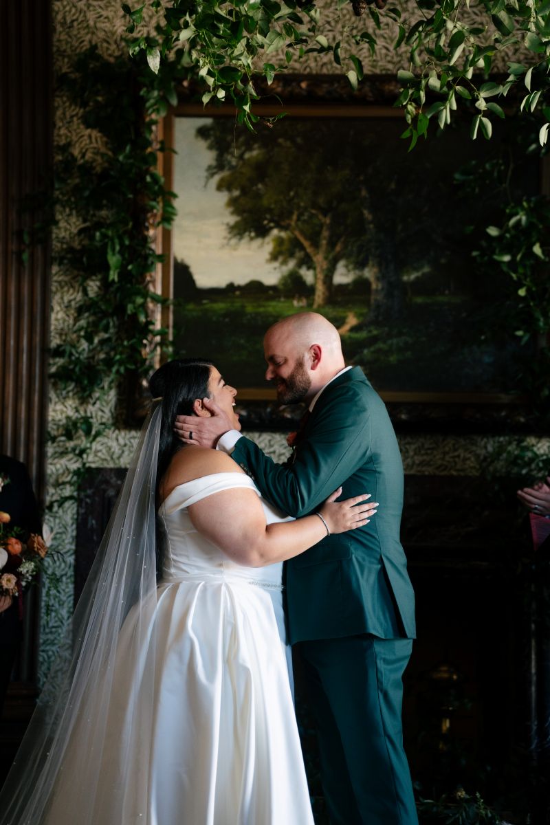 a couple smiling and laughing together during their wedding ceremony the man has his hands on his partner's cheeks the woman is touching his side