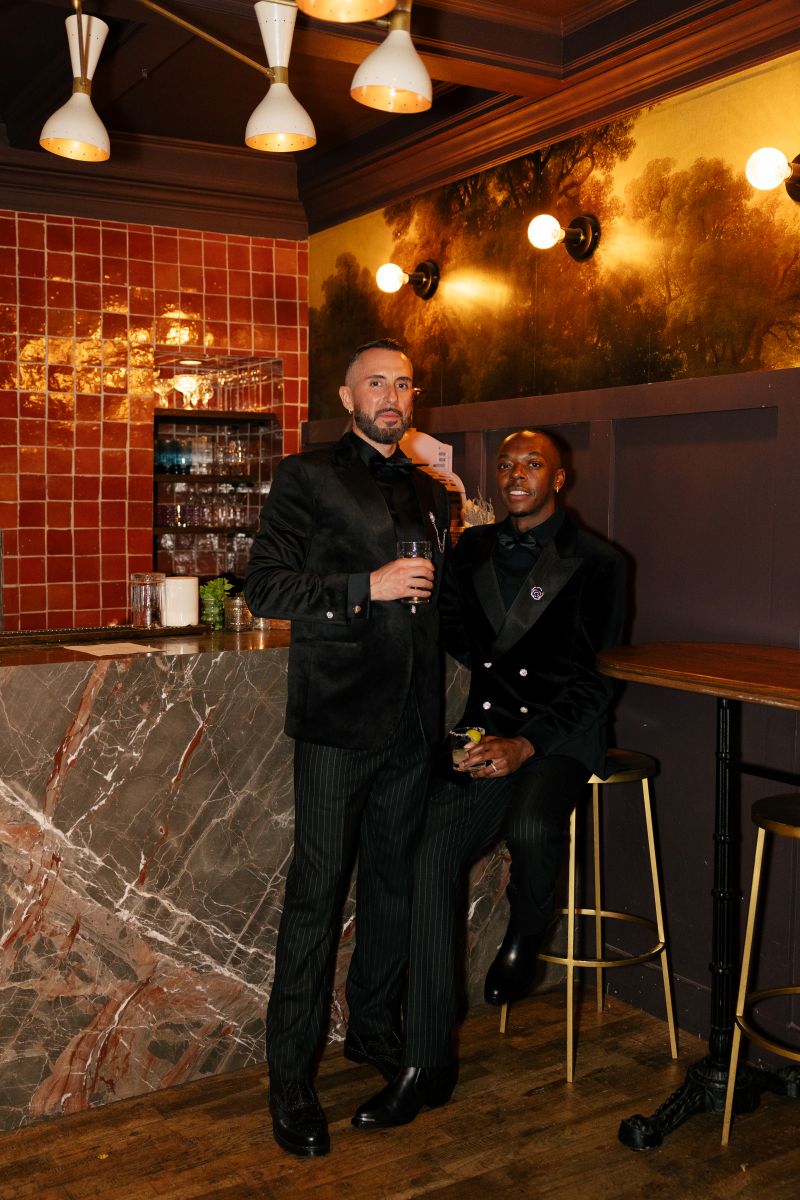 a couple sitting on the bar stool inside of fiorella sunset for their wedding reception they are wearing matching black suits