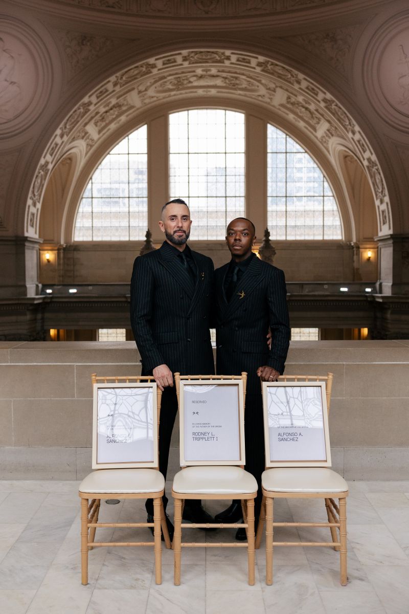a couple standing side by side in front of three chairs on the 4th floor of san francisco city hall