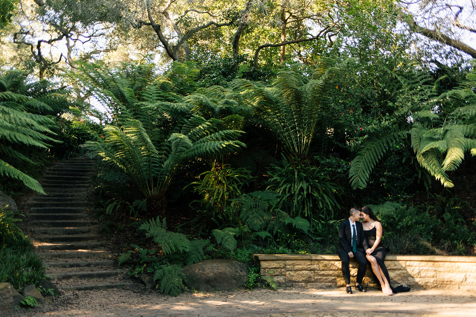 a couple wearing all black taking engagement pictures at aids memorial grove inside golden gate park 