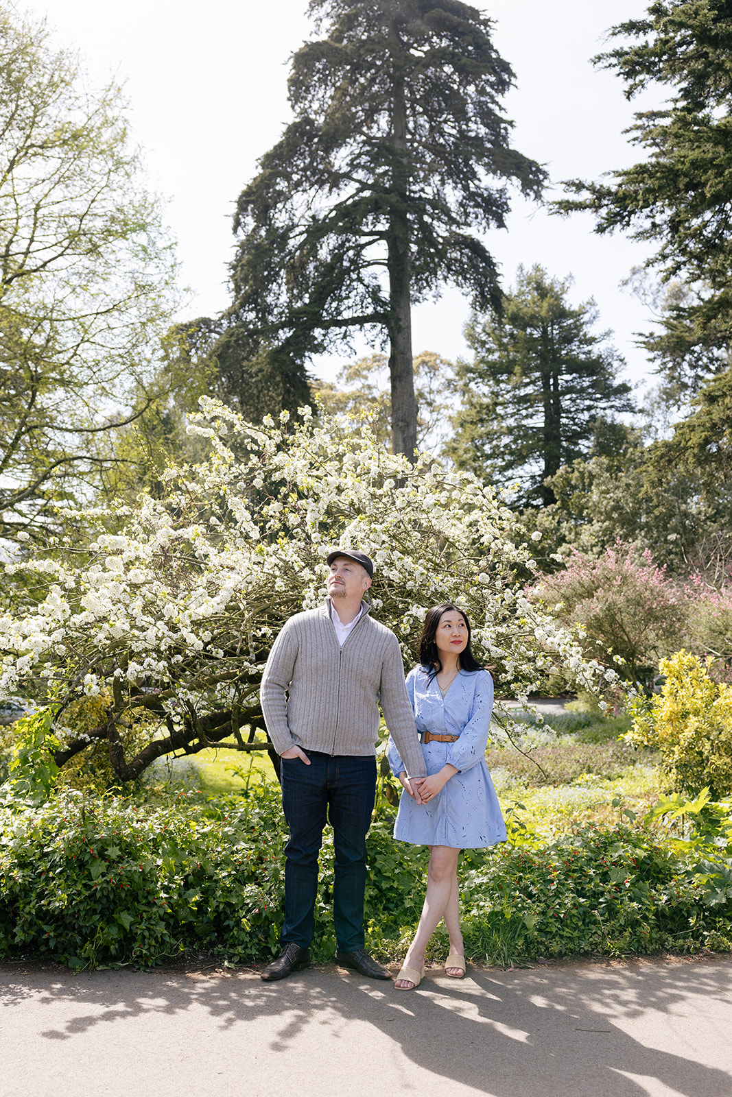 a couple taking engagement pictures, holding hands and looking in opposite directions at stow lake inside of golden gate park 