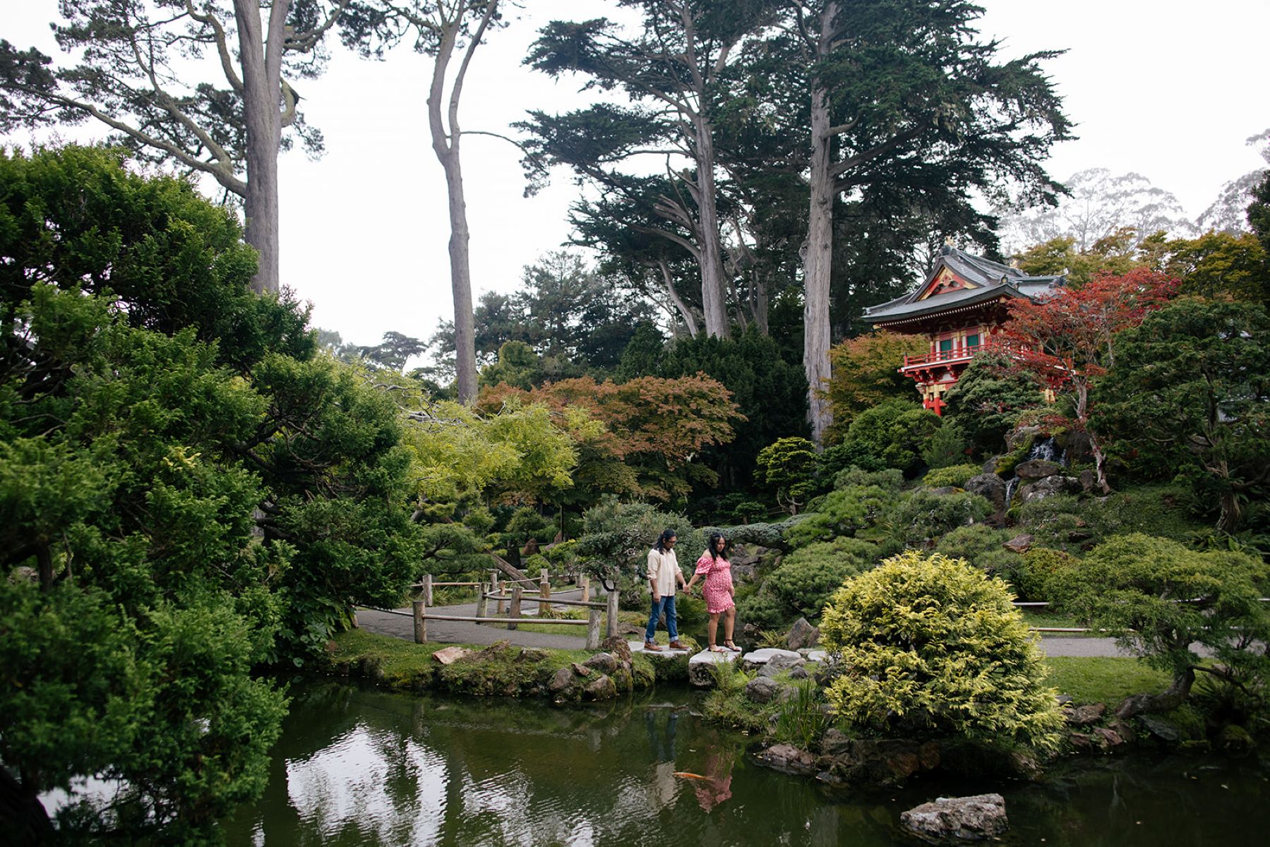 a couple walking hand in hand through the japanese tea garden inside of golden gate park next to a koi fish pond 
