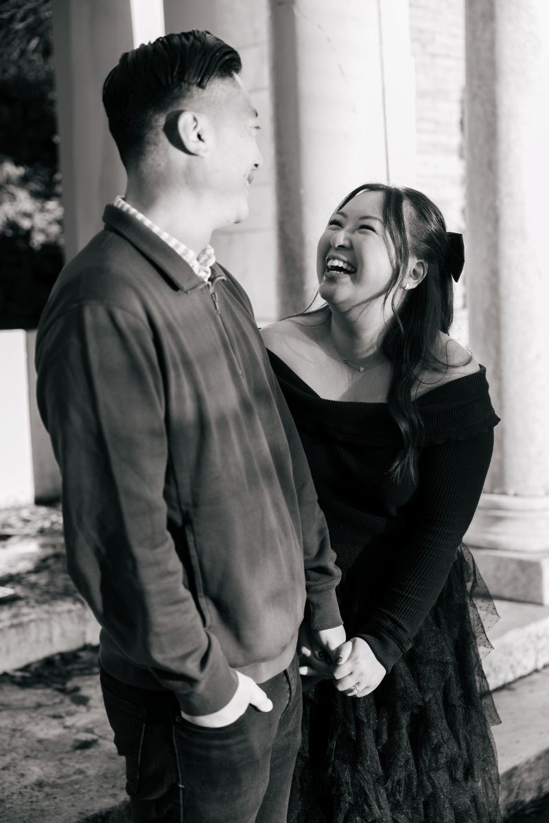 a couple taking engagement pictures at portals of the past inside of golden gate park they are both holding hands and laughing with each other 
