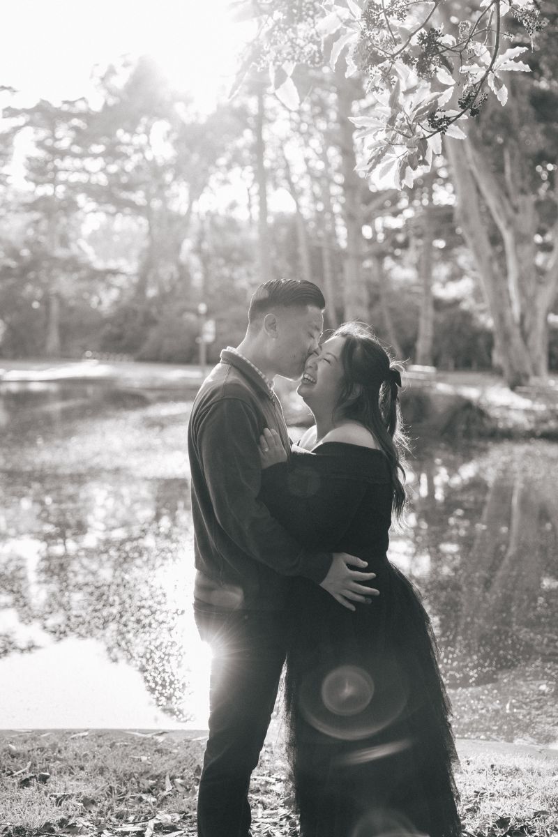 a couple taking engagement pictures at portals of the past inside of golden gate park the man is embracing his partner around the waist and leaning in to kiss her 
