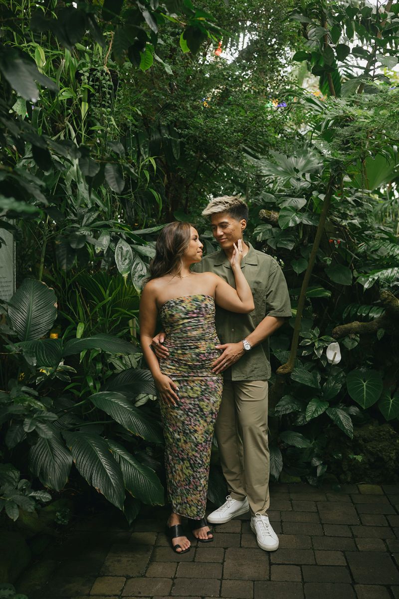 a couple taking engagement pictures in front of a variety of green plants inside of the Conservatory of Flowers in golden gate park 