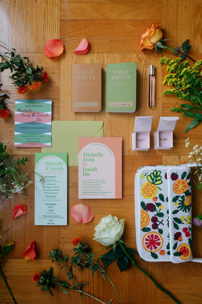 Wedding invitations, notebooks, rings, a purse, and floral clippings laid out in a wedding flat lay photo 