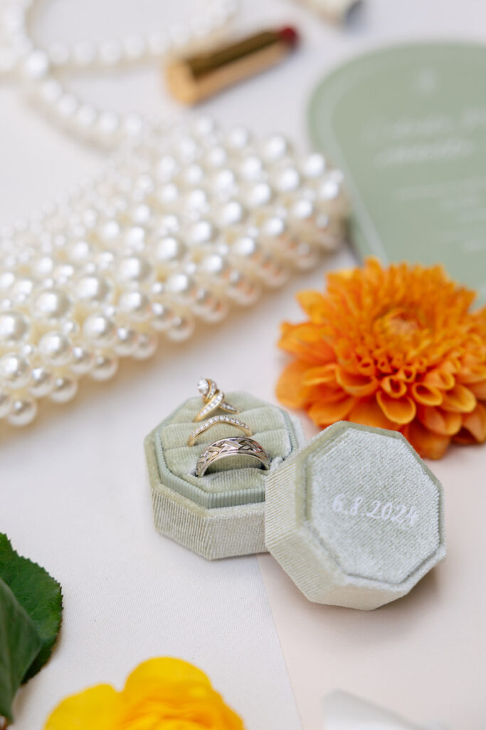 Wedding and engagement rings in a ring box next to jewelry and flowers 