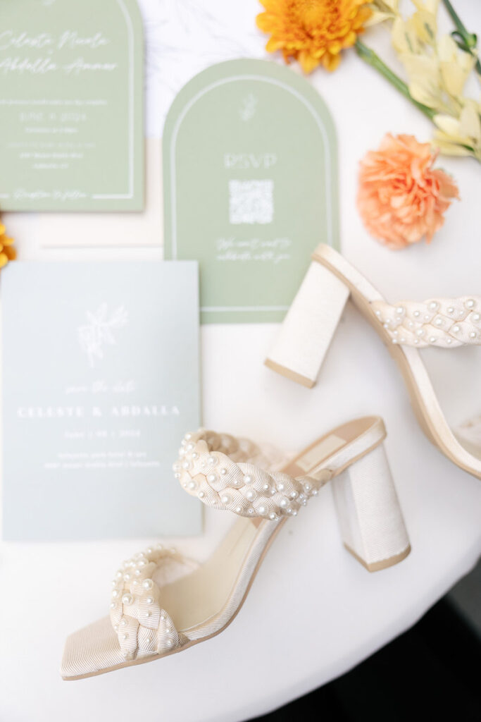 Wedding invitations, colorful flowers, and white heels laid on a table 
