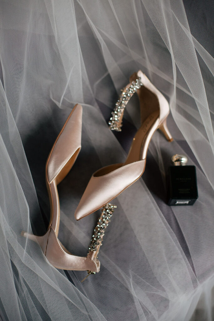 Tan heels and a perfume bottle laid on top of a veil 
