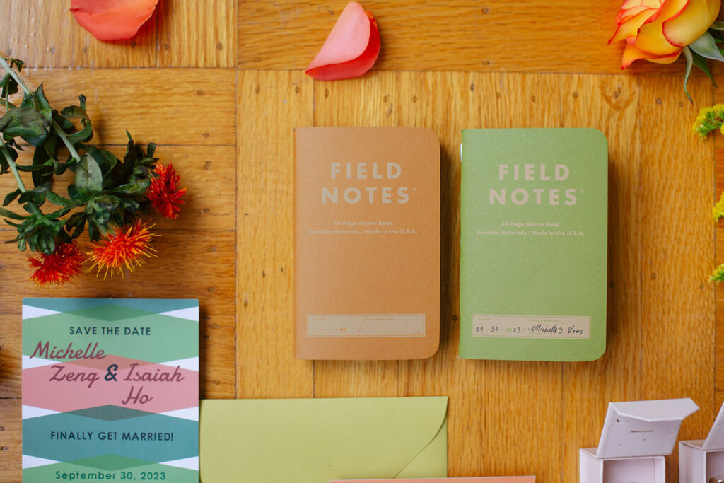 Two small notebooks laid on a table with wedding invitations 