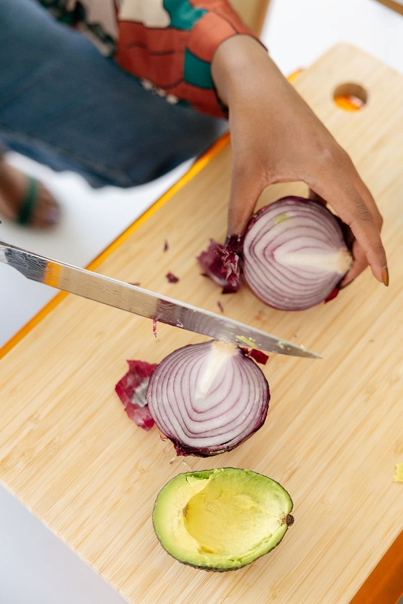 a woman cutting onions on top of a cutting board there is also an avocado on the cutting board