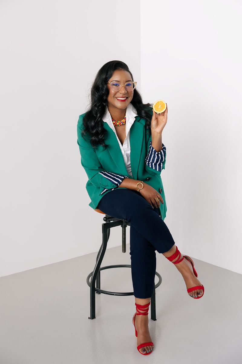the owner of ebb and flow nutrition and consulting sitting on a stool with her legs crossed and is holding a lemon