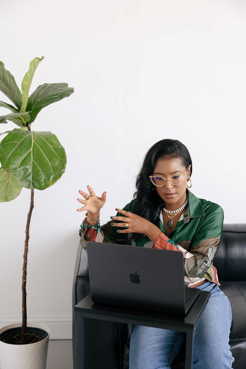 the owner of ebb and flow nutrition and consulting sitting on a black leather couch and talking on a call to a client on her laptop