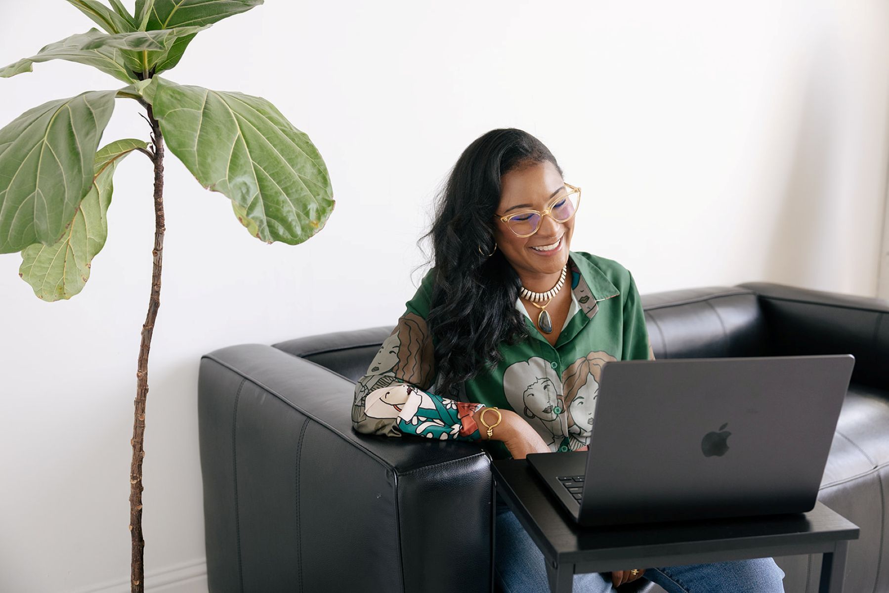 the founder of ebb and flow nutrition and consulting sitting on a black leather couch smiling and looking at her laptop