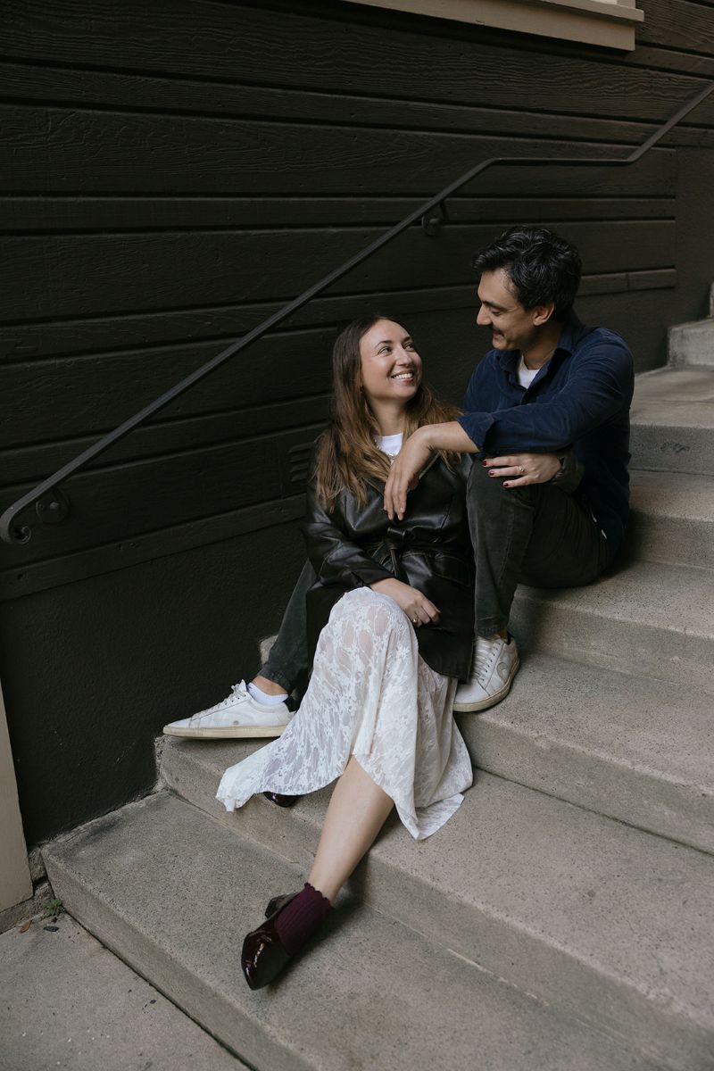a couple sitting on cement steps touching one another and smiling at one another