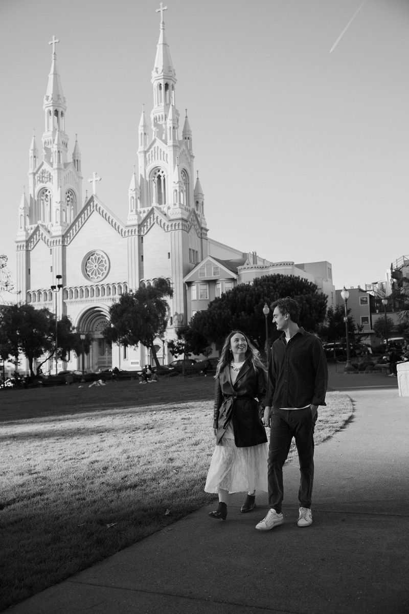 a couple walking hand in hand down a sidewalk with st peter and paul church in north beach behind them