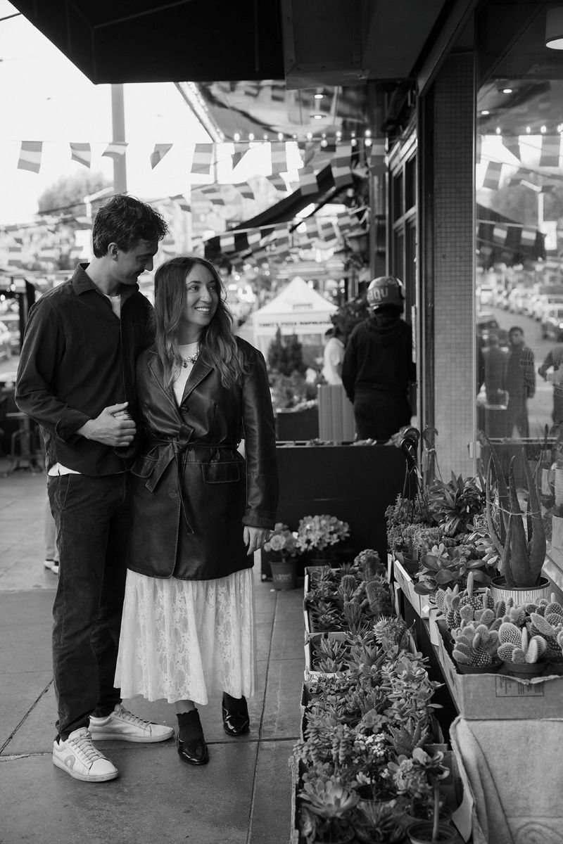 a copule pausing at a flower shop and admiring the plants together