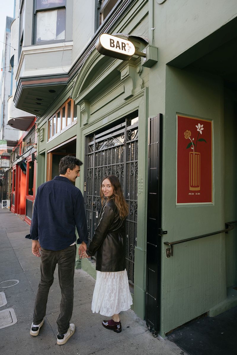 a couple holding hands and walking down a street in north beach