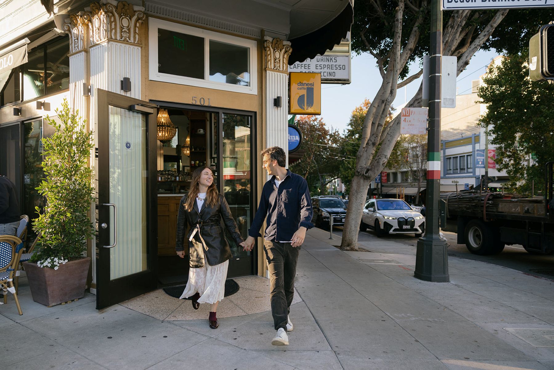 a couple walking hand in hand together in front of a store smiling at each other in north beach