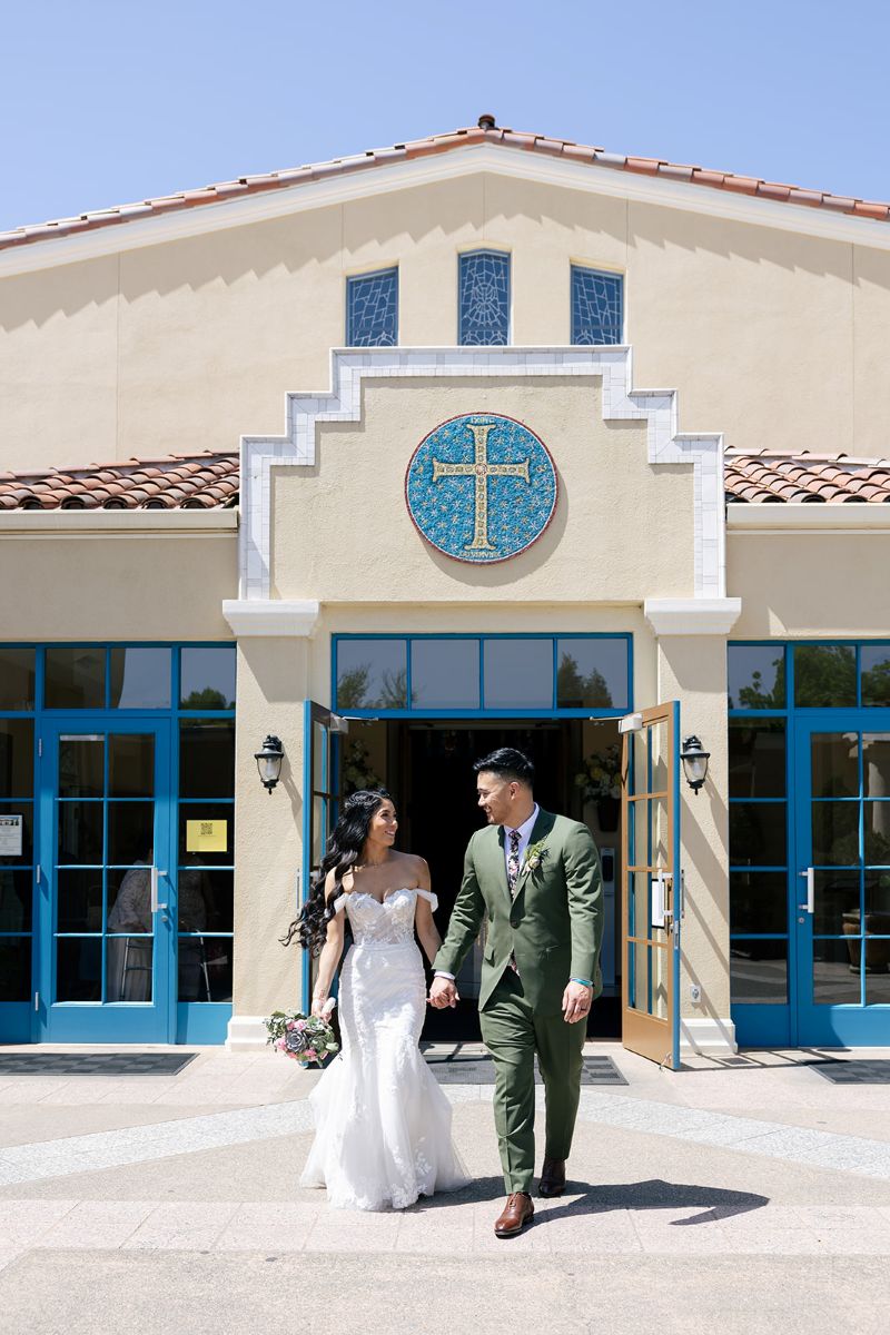 a couple waking hand in hand out the doors of Apollinaris Catholic Church after their wedding ceremony