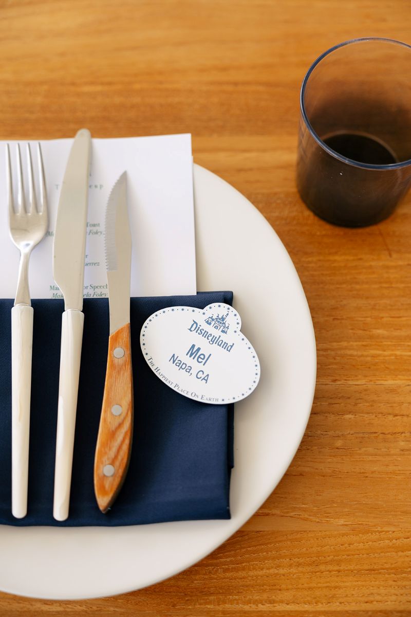 a plate on top of a wooden table set up for a wedding reception with cutlery and a wedding invitations 