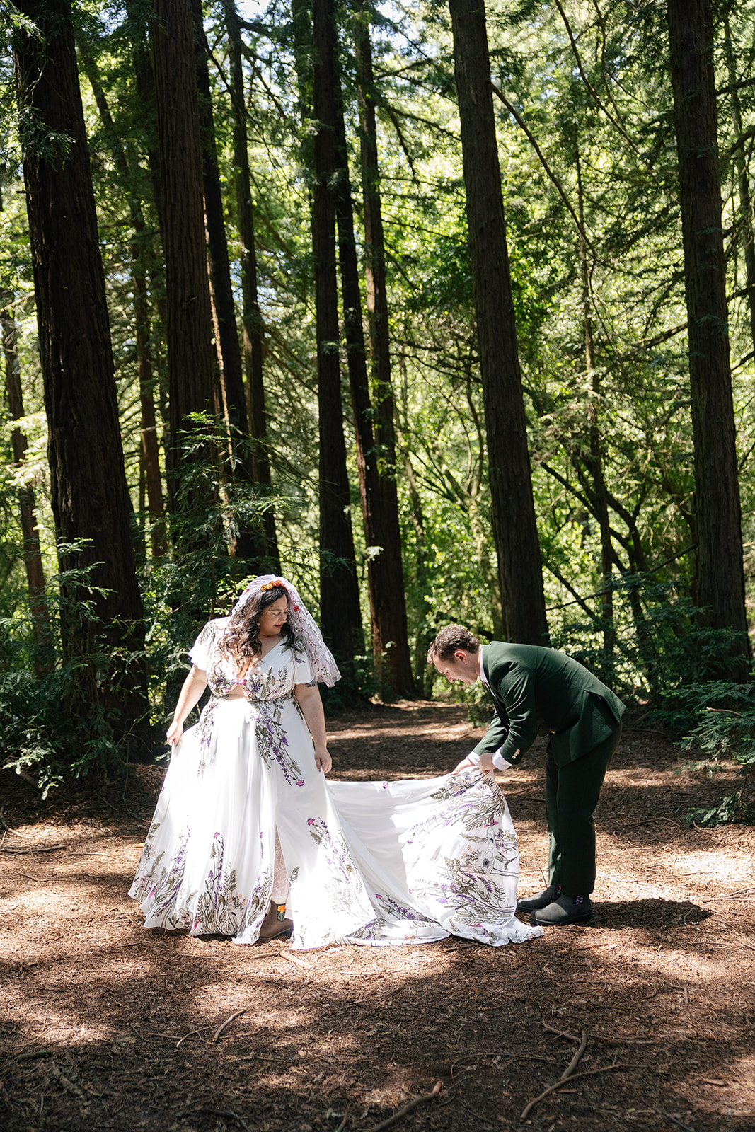a groom helping his bride with her wedding dress standing in the forest in roberts regional park 