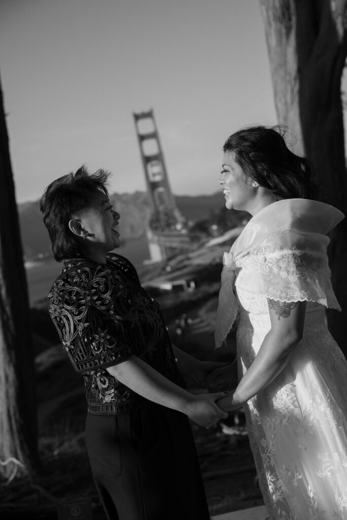 a wedding couple holding hands and laughing with the golden gate bridge behind them